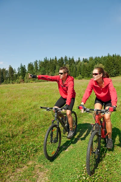 Genç çift sürme dağ bisikleti bahar çayırda — Stok fotoğraf