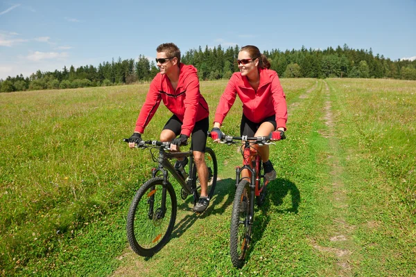 Young couple riding mountain bike in spring meadow — Stock Photo, Image