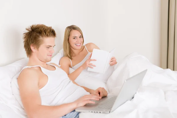 Dormitorio - pareja joven con ordenador portátil y libro — Foto de Stock