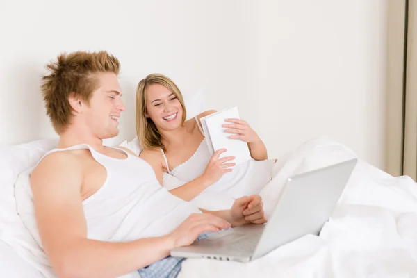 Dormitorio - pareja joven con ordenador portátil y libro — Foto de Stock