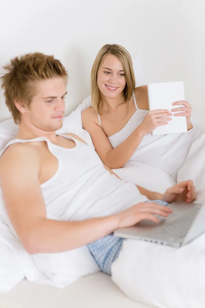 Camera da letto - giovane coppia con computer portatile e libro — Foto Stock