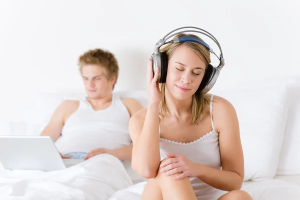 年轻夫妇放松躺在床上与音乐和便携式计算机 — 图库照片