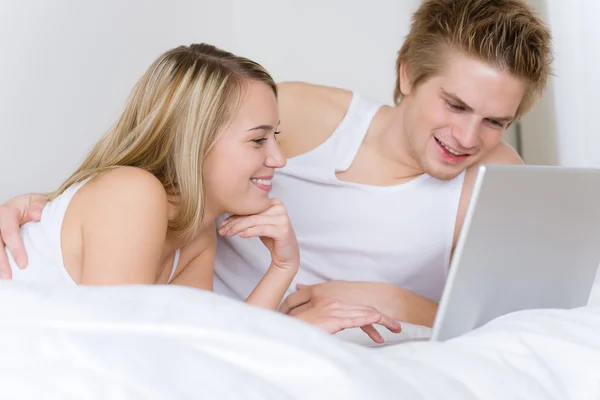 Νεαρό ζευγάρι χαλαρώσετε στο κρεβάτι με το lap-top — Φωτογραφία Αρχείου