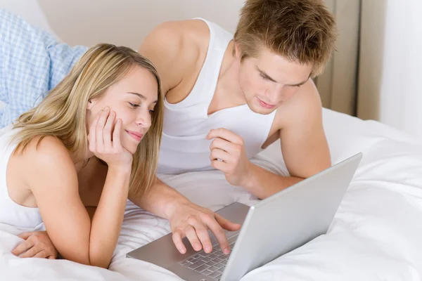 Jovem casal relaxar na cama com laptop — Fotografia de Stock