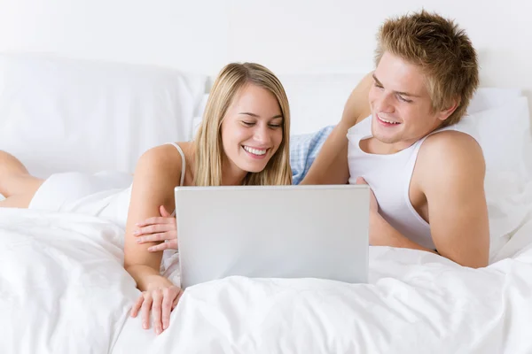 Jovem casal relaxar na cama com laptop deitado — Fotografia de Stock