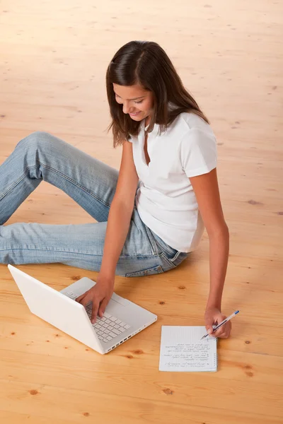Lächelnder Teenager Sitzt Mit Laptop Und Schreibt Notizen Auf Holzboden — Stockfoto
