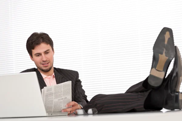 成功的现代商人与便携式计算机和坐在办公室的报纸 — 图库照片