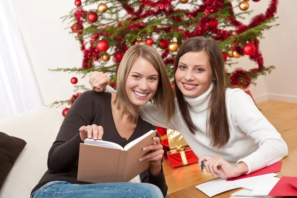 Δύο Νεαρών Γυναικών Γράφοντας Κάρτες Χριστουγέννων Μπροστά Από Δέντρο — Φωτογραφία Αρχείου
