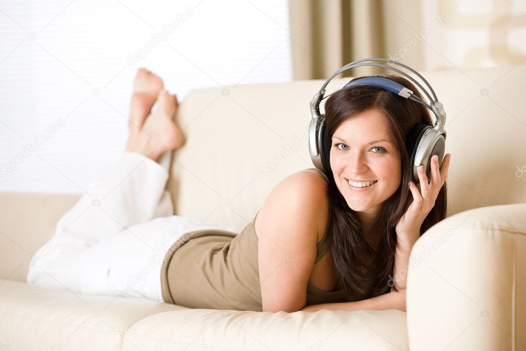 Happy woman with headphones lying down on sofa in lounge