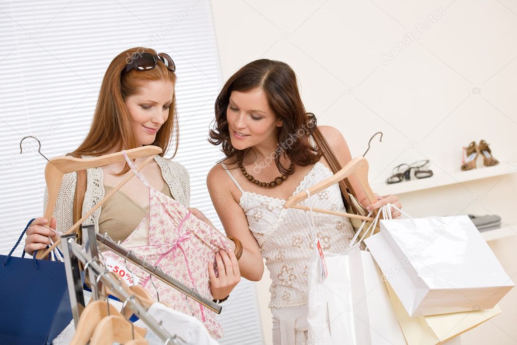 Fashion shopping - Two happy young woman choose clothes in shop holding shopping bag