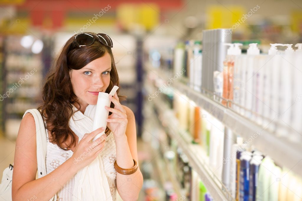 Shopping cosmetics - woman smelling bottle of shampoo in drug-store