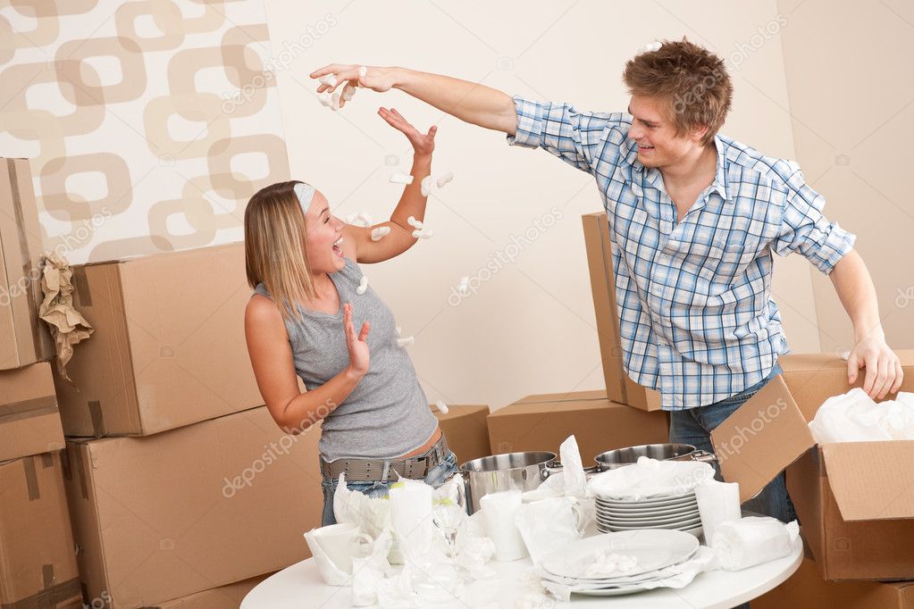 Moving house: Man and woman having fun while unpacking box with kitchen dishes