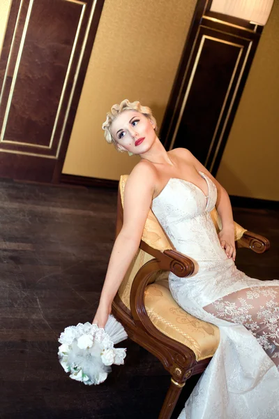 Bruid blond met een boeket zit op een stoel — Stockfoto