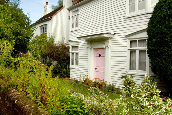 Wooden cottage in great britain or england. small wood house with garden in front and pink door.cosy historic homes in village location