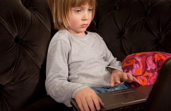 stock image Child sitting with laptop computer on sofa in the evening playing. domestic environment with boy using technology