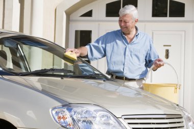Senior man wasing car with sponge outside house clipart