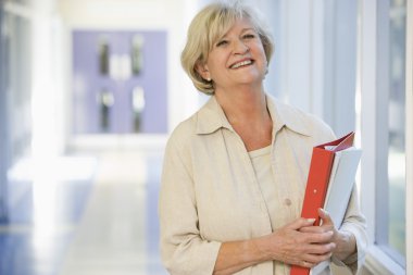 A woman with a ringbinder standing in a campus corridor clipart