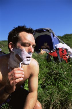 Man shaving in the outdoors next to tent clipart