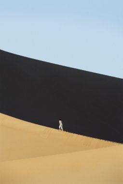 Woman walking across desert sand dunes clipart