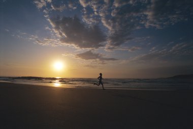 Person running along beach at sunset clipart