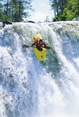 Young man kayaking down waterfall clipart