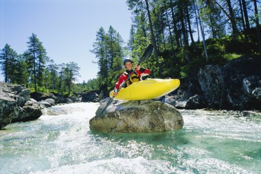 Kayaker perched on boulder in river clipart