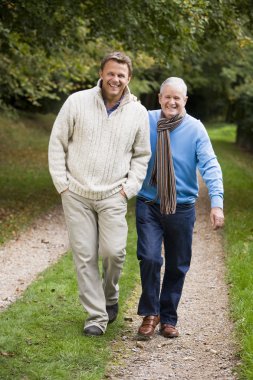 Adult father and aon walking along woodland path in autumn clipart