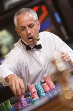 Man placing bet at roulette table in casino clipart