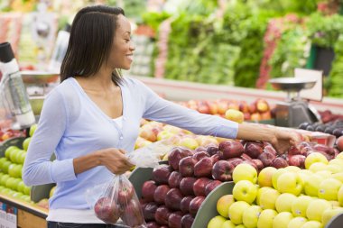 Young woman shopping in produce section of supermarket clipart