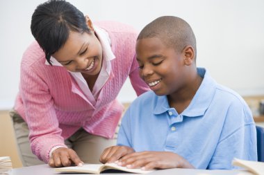 Elementary school teacher helping pupil with reading clipart