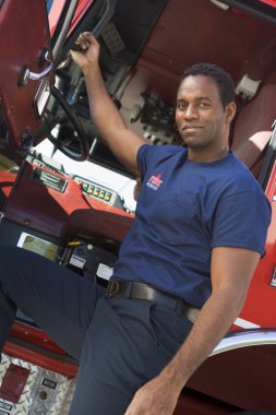 A firefighter standing by the cab of a fire engine clipart