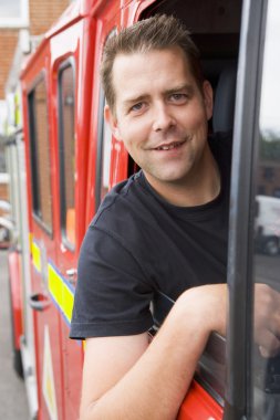 Male firefighter sitting in the cab of a fire engine clipart