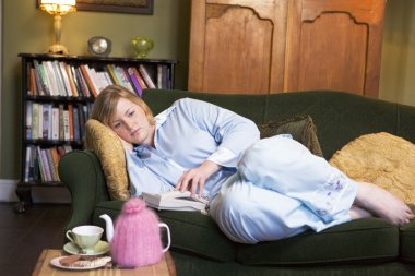 A young woman lying on her couch reaching for the phone clipart