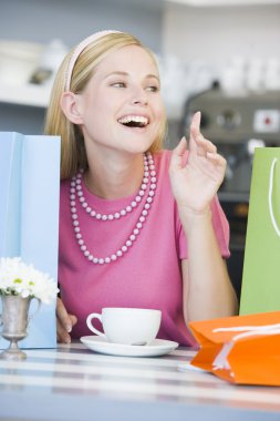 A young woman sitting in a cafe with shopping bags clipart