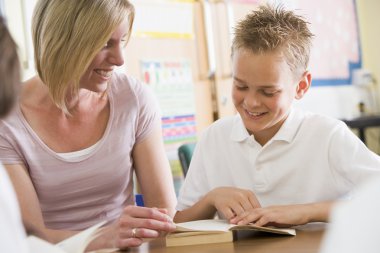 A schoolboy and his teacher reading a book in class clipart