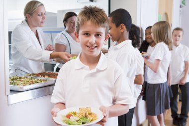 Schoolboy holding plate of lunch in school cafeteria clipart