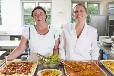 Lunchladies beside trays of food in school cafeteria clipart