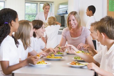 Teacher and schoolchildren enjoying their lunch in a school cafe clipart