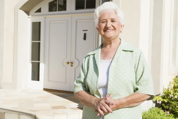 Senior woman standing outside front door of house