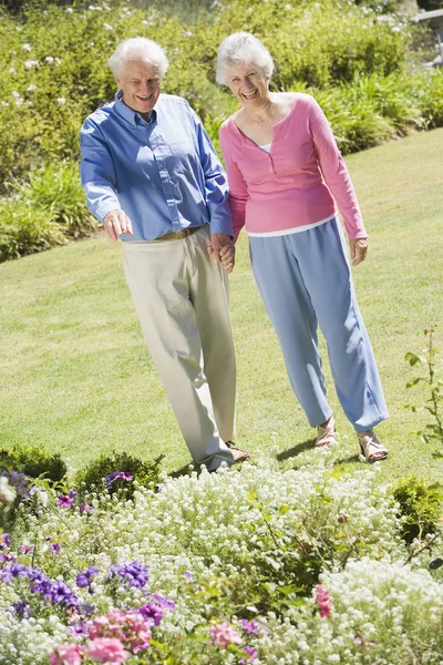 花壇に見とれながら庭を歩いて年配のカップル — ストック写真