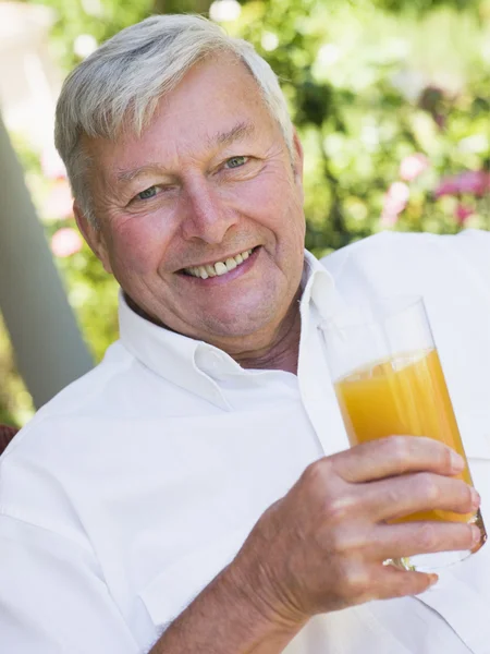 高级享受杯橙汁 坐在花园的位子上的男人 — 图库照片