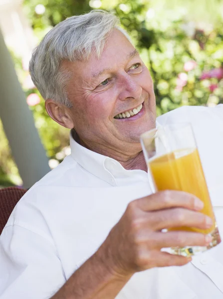庭座席に座っているジュースのグラスを楽しむシニア男性 — ストック写真