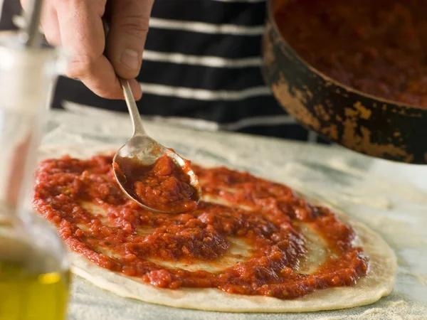 男子用勺子挖到一个披萨基地上的番茄汁 — 图库照片
