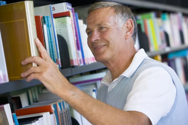 Старший чоловік витягує бібліотечну книгу з полиці — стокове фото