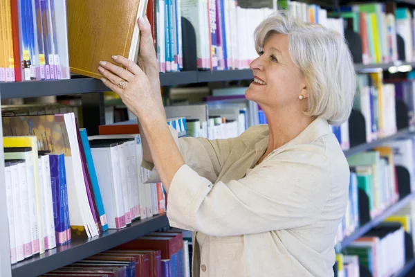 Femme âgée tirant un livre de bibliothèque sur étagère — Photo