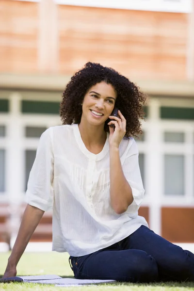 Жінка на мобільному телефоні сидить на галявині кампусу — стокове фото