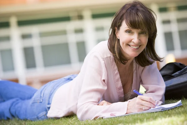 キャンパスの芝生の上に横たわっている間ノートを書く女 — ストック写真