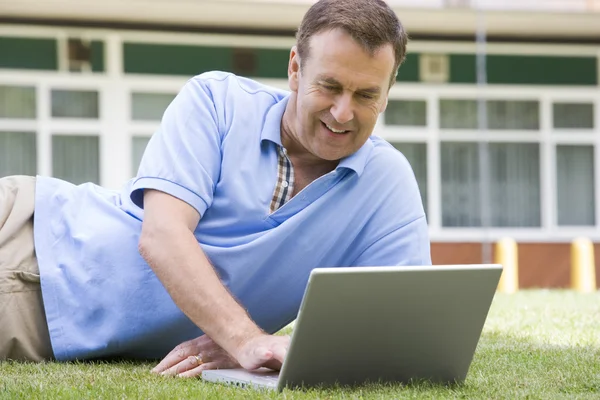 男子躺在草地上校园的同时使用笔记本电脑 — 图库照片