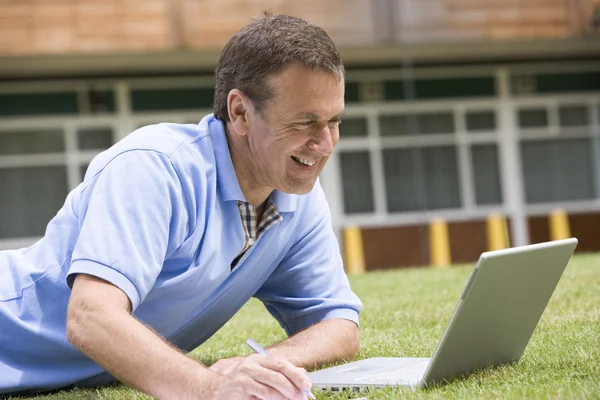 男子躺在草地上校园的同时使用笔记本电脑 — 图库照片