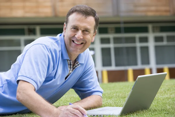 Człowiek za pomocą laptopa leżąc w trawie na kampusie — Zdjęcie stockowe